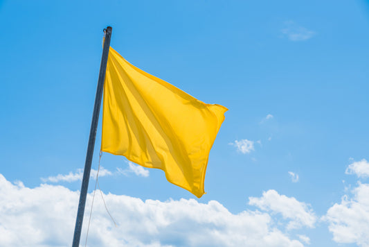 Yellow flag on a pole against a blue sky with some clouds